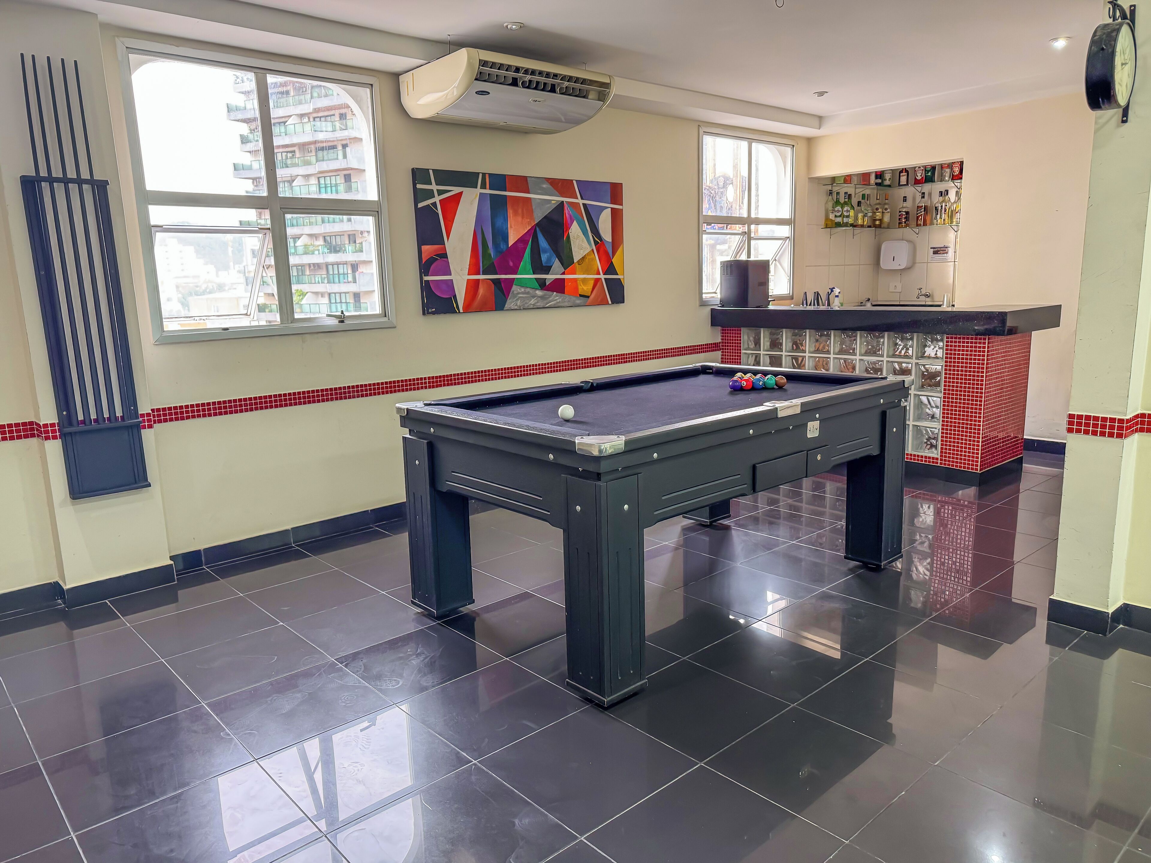A pool table with balls, a colorful abstract painting, and a bar area with liquor bottles.