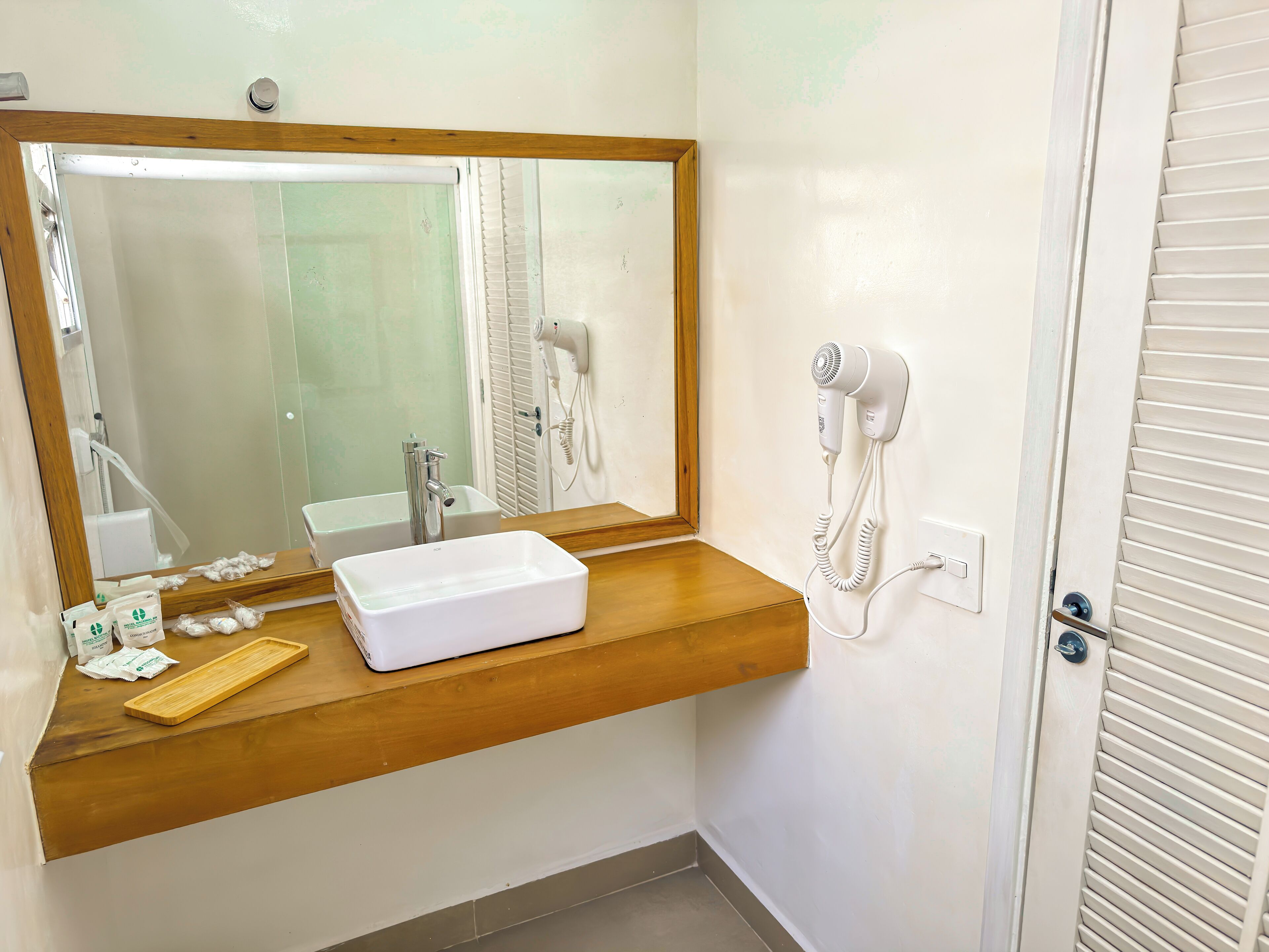 Ein Badezimmer mit einem Holzkosmetikschrank, einem großen Spiegel, einem Föhn und einem Waschbecken.
