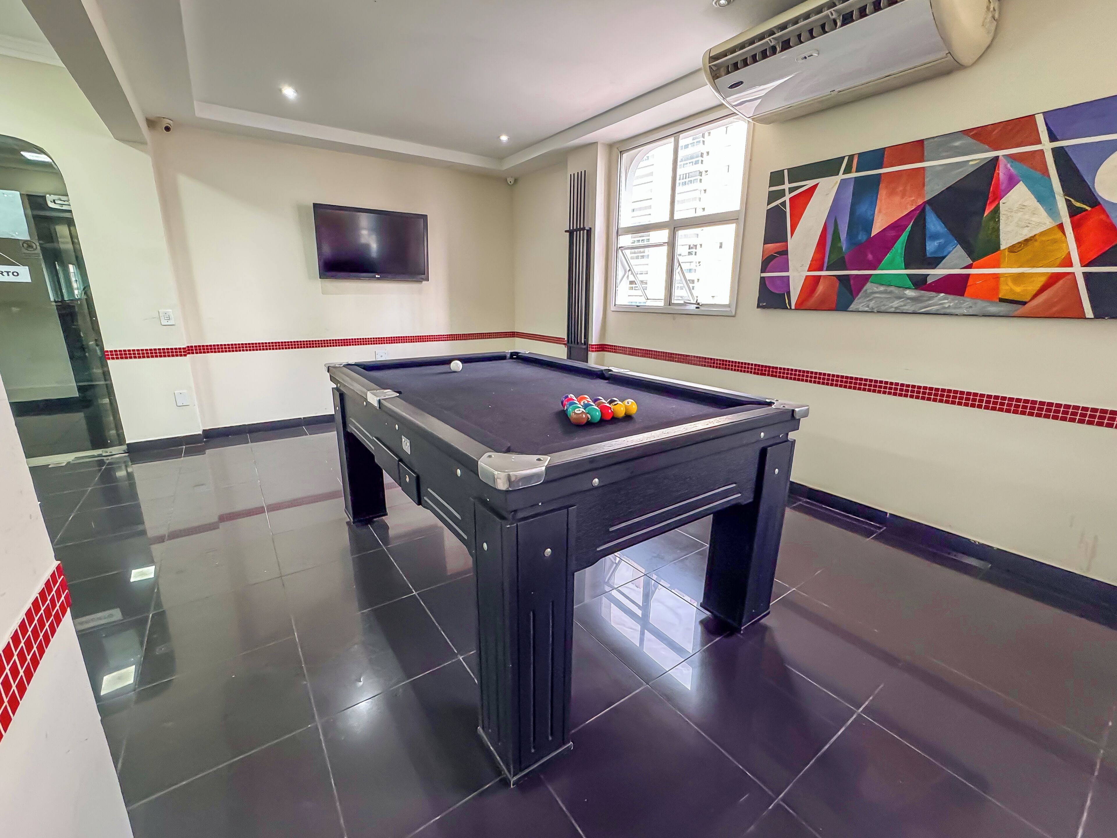 A pool table with balls, a television, and a colorful abstract painting on the wall.