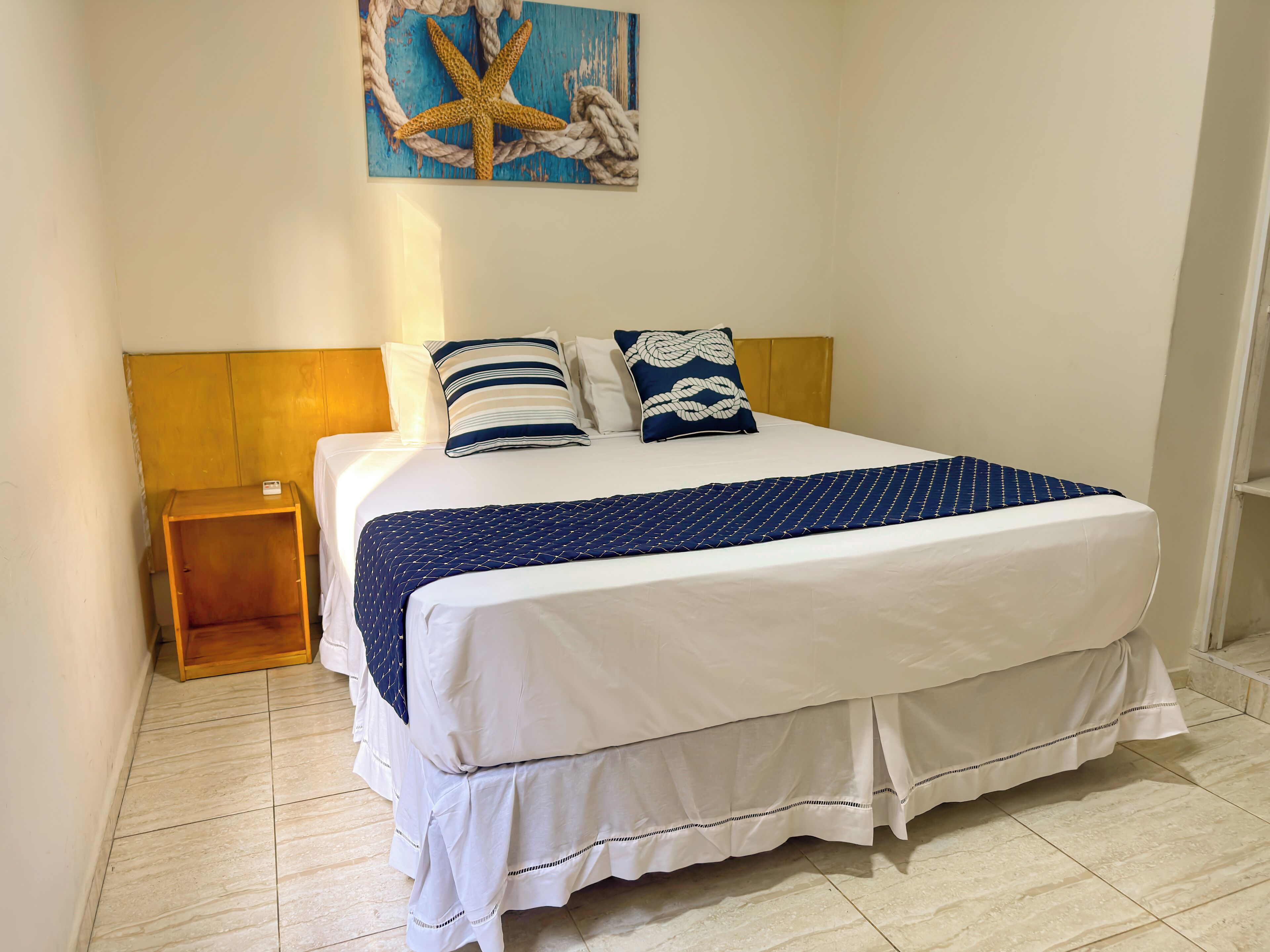 A neatly made bed with white and navy blue bedding, a wooden headboard, and a small wooden nightstand beside it.