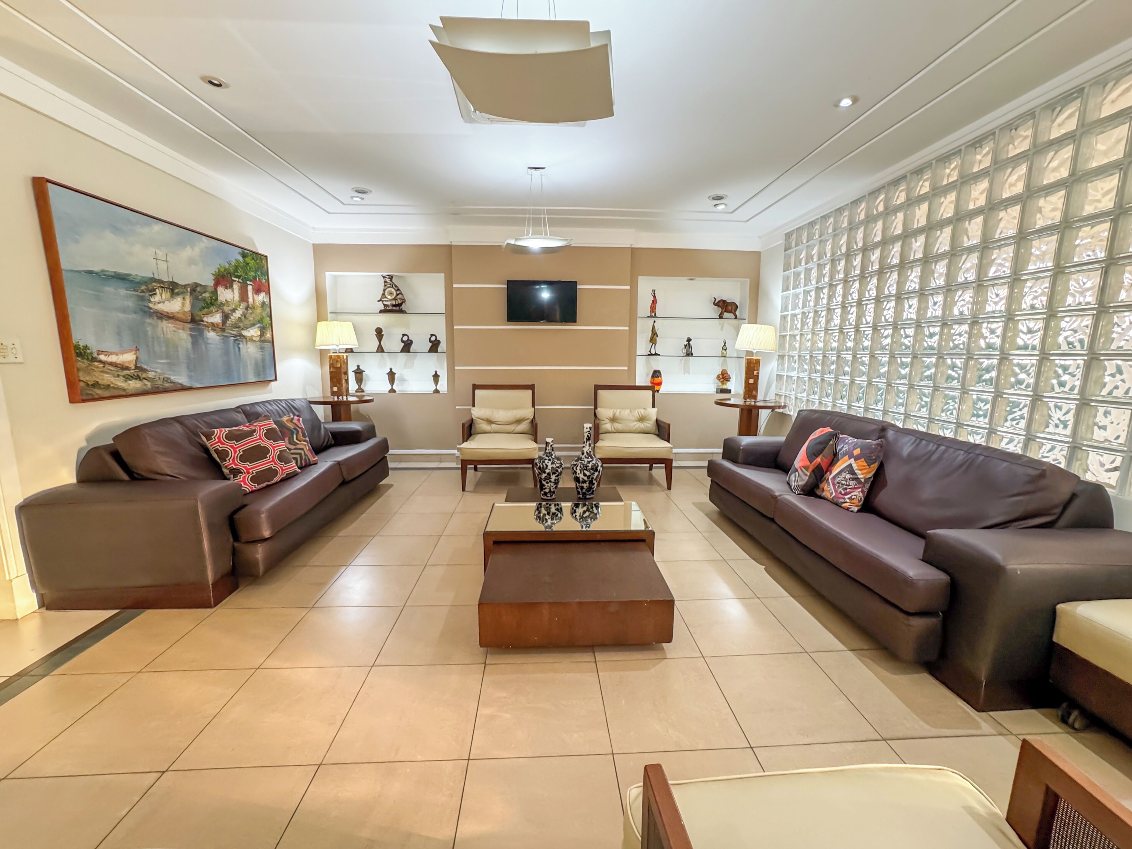 Amplia sala de estar con dos sofás, una mesa de centro, un televisor y objetos decorativos en estantes.