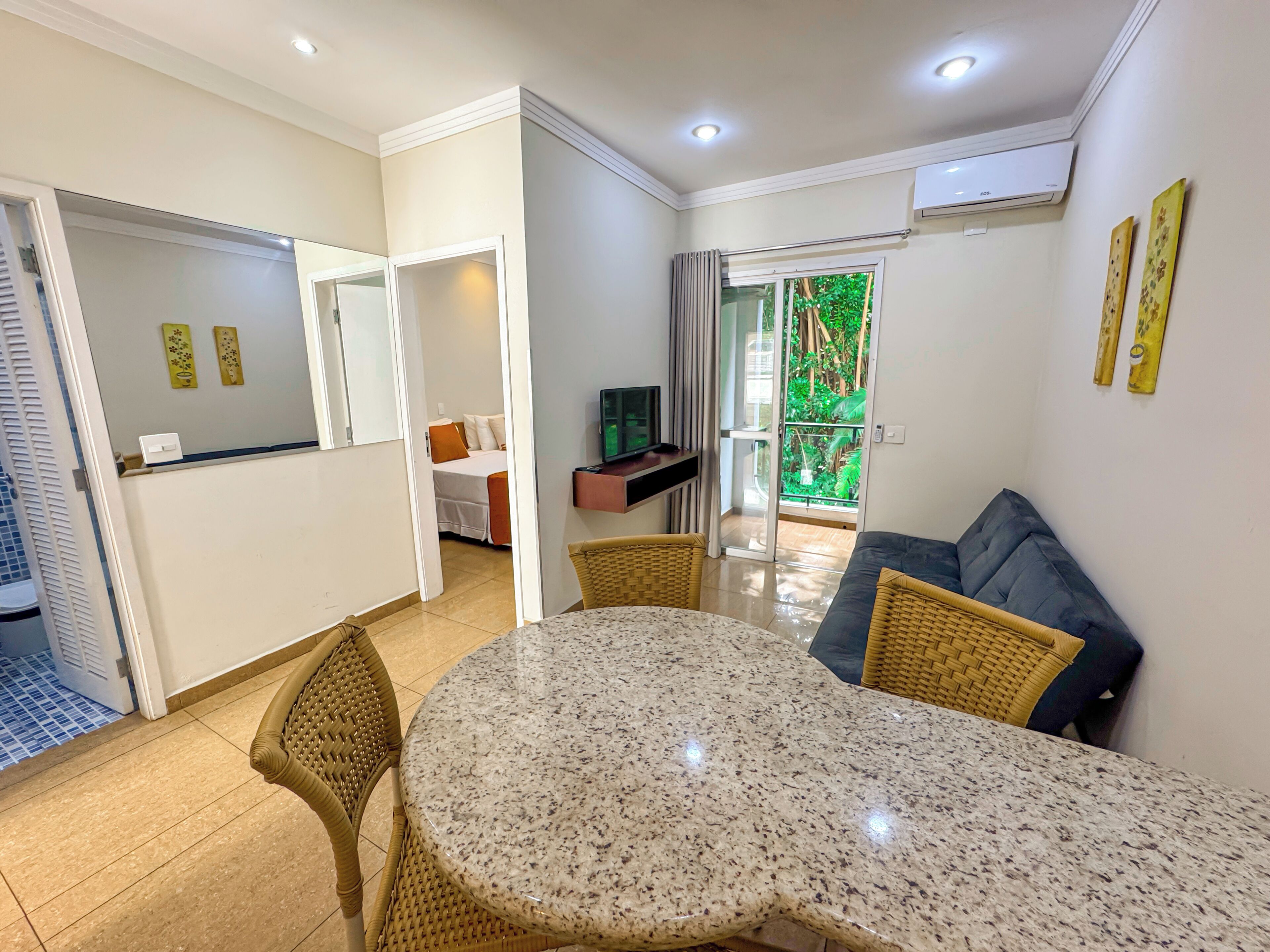 A modern living room with a round table, wicker chairs, a sofa, and a TV on a stand.