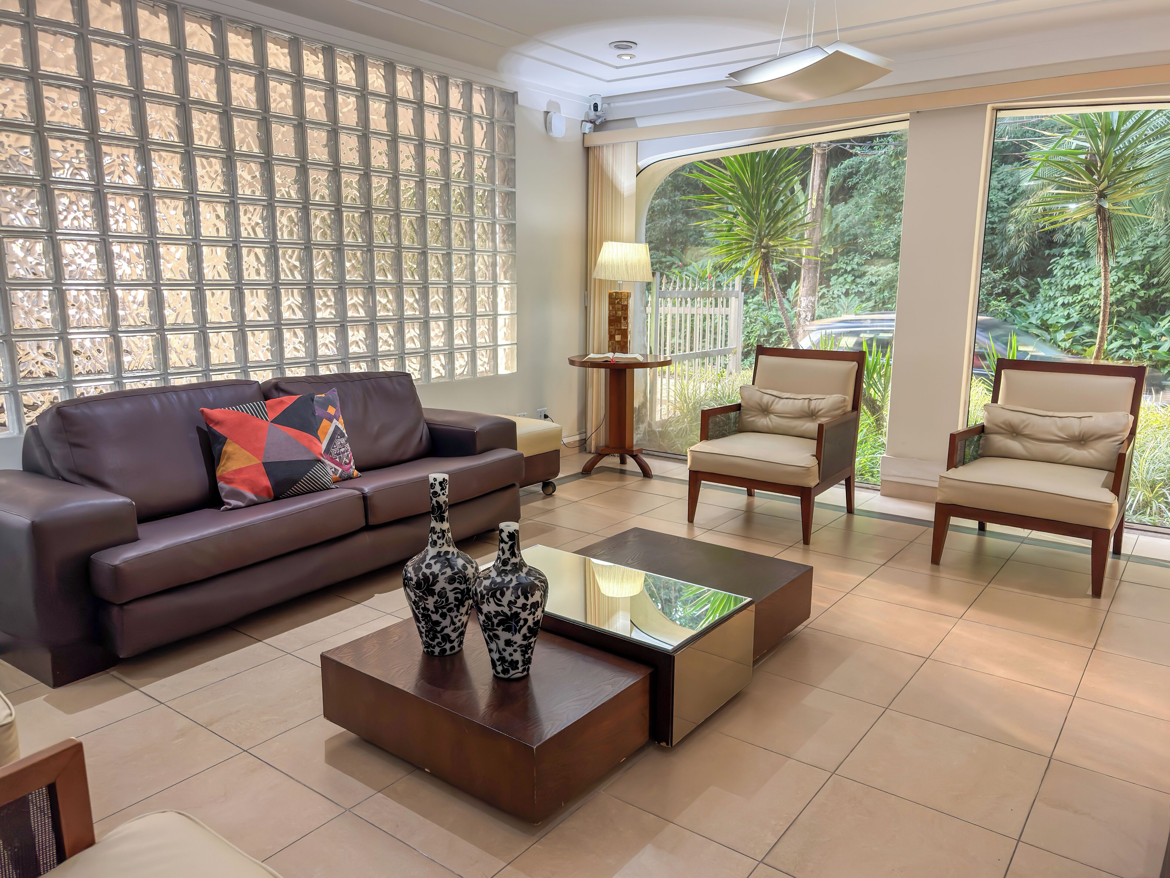 Una sala de estar moderna con un sofá de cuero marrón, dos sillones color beige, una mesa de centro de vidrio y un jarrón decorativo.