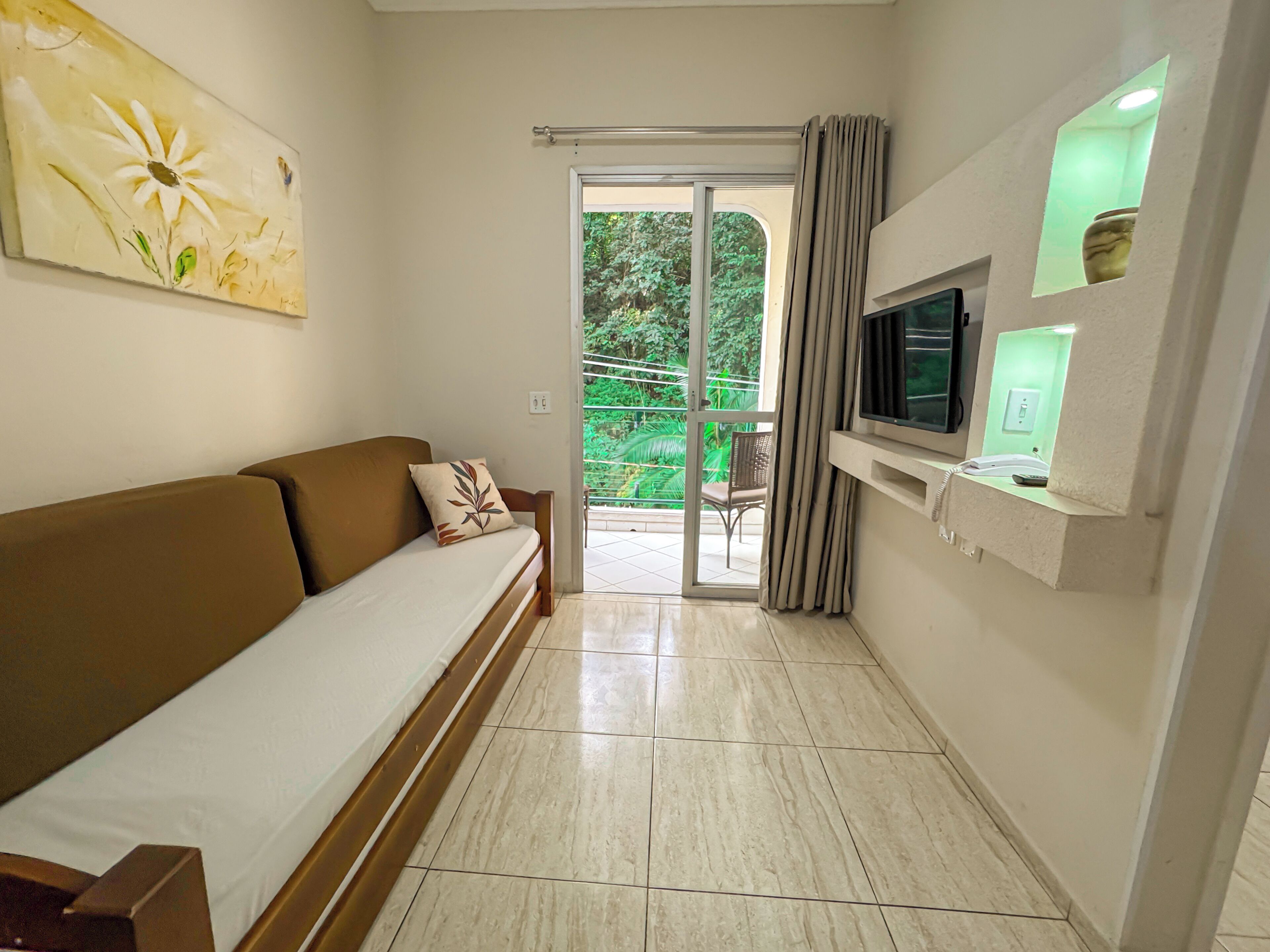 A modern living room with a sofa, a TV, and a sliding glass door leading to a balcony.