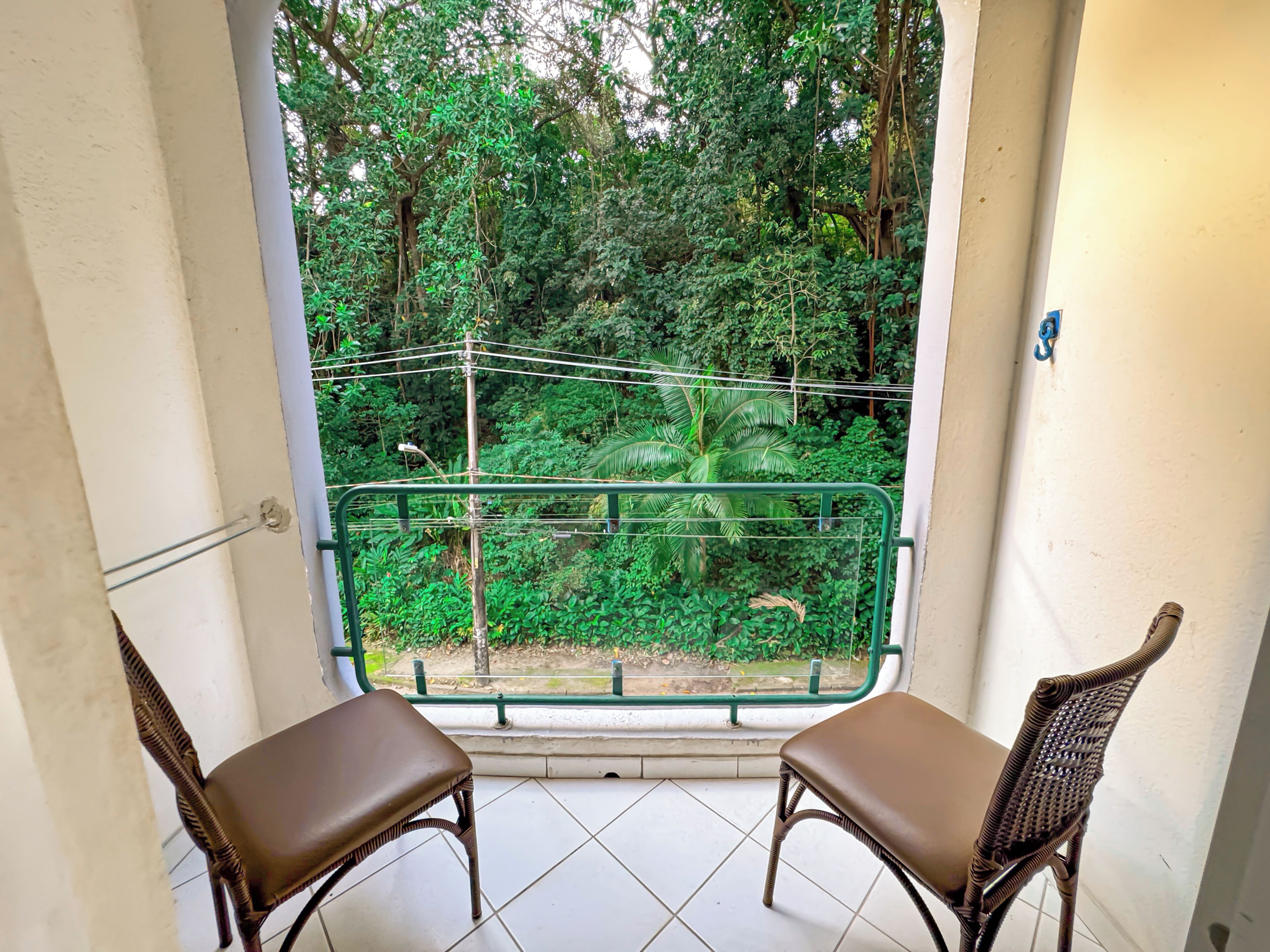 A balcony with two wicker chairs and a view of dense greenery.