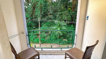A balcony with two wicker chairs and a view of dense greenery.