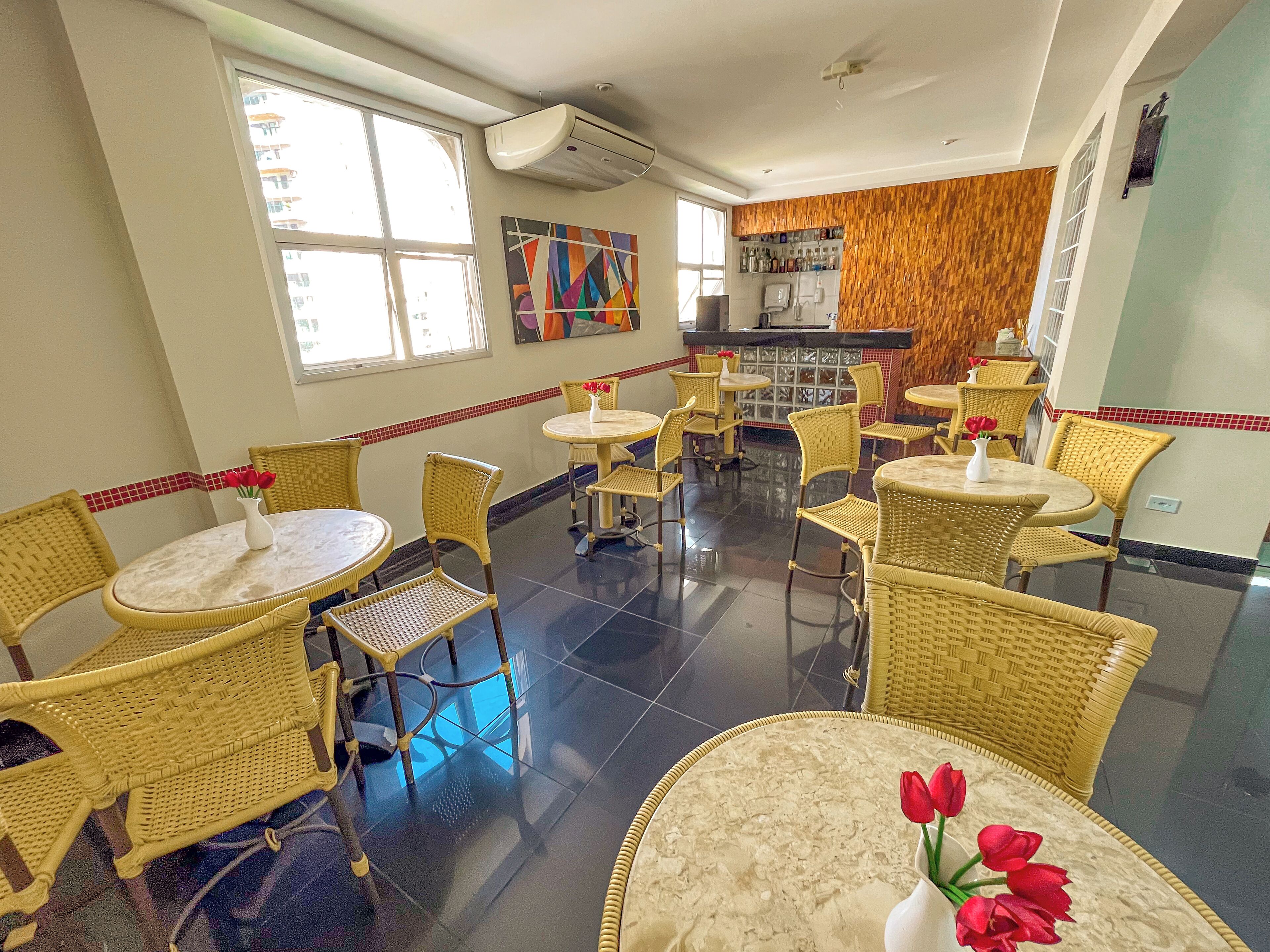 A restaurant with wicker chairs and tables, a tiled floor, and a bar area with a wooden wall.