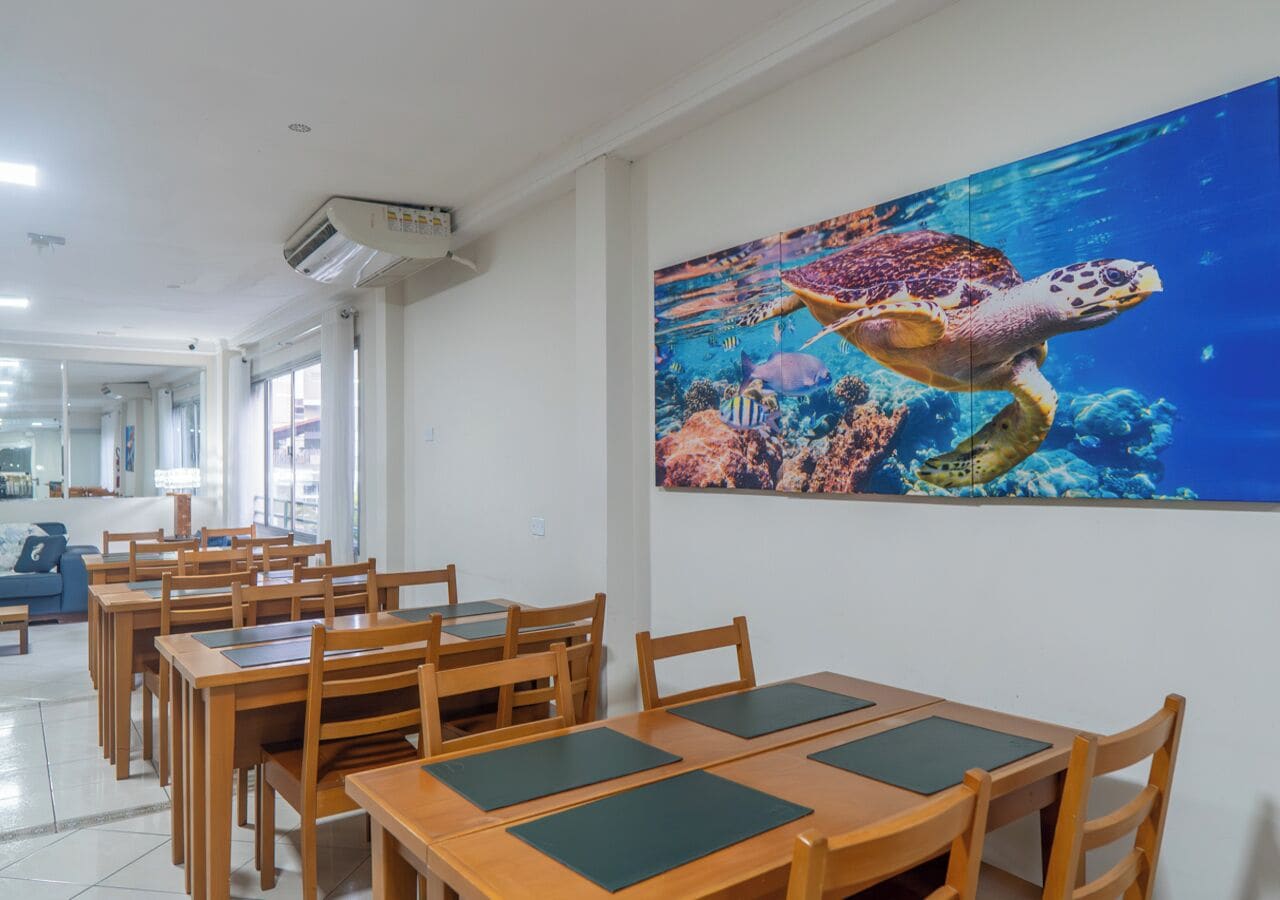 Un comedor con mesas y sillas de madera, un gran mural de una tortuga marina en la pared, y un diseño interior moderno.