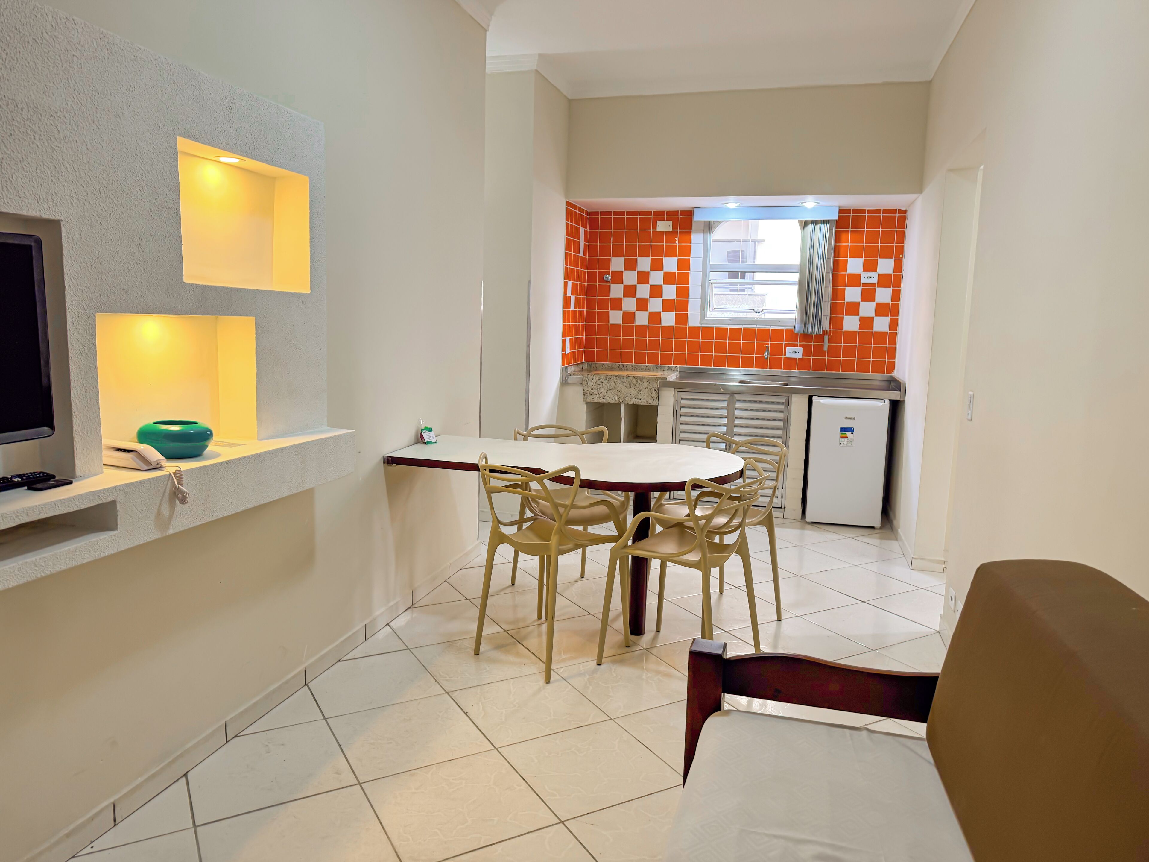 A compact living space with a dining area, kitchenette, and a TV on a shelf.