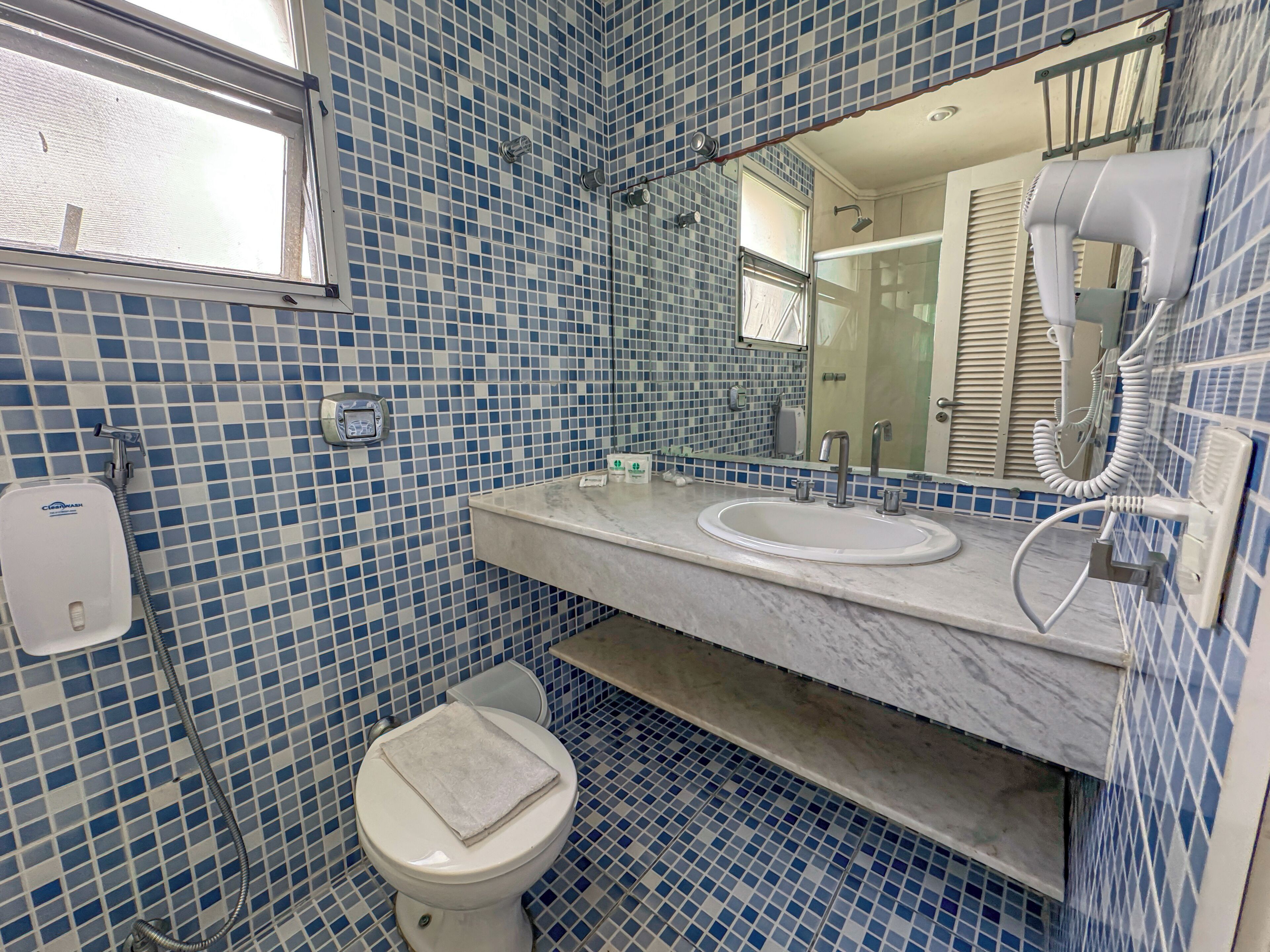 Un baño con suelo de baldosas, lavamanos, inodoro y espejo.
