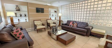 A modern living room with a brown leather sofa, two armchairs, a coffee table, and a TV mounted on the wall.
