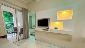 A modern living room with a flat-screen TV, a small shelf with decorative items, and a dining area with a table and chairs. - Hotel Nacional Inn Guarujá (Guarujá)