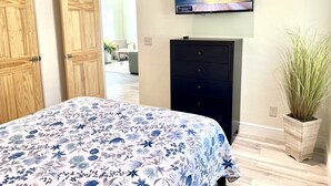 A bedroom with a bed, a TV mounted on the wall, a dresser, and a potted plant. - Home Sweet Home (Sanford)