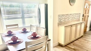 A dining area with a wooden table set for four, a refrigerator, and a kitchen with a tiled backsplash and wooden cabinets. - Home Sweet Home (Sanford)