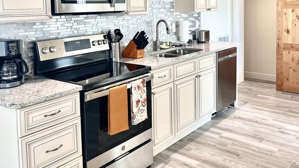 A modern kitchen with light-colored cabinets, stainless steel appliances, and a herringbone-patterned backsplash. - Home Sweet Home (Sanford)