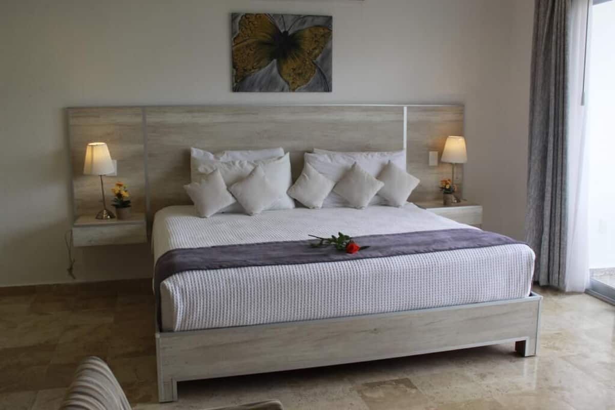 Un dormitorio ordenado con una cama grande, dos mesitas de noche con lámparas y una obra de arte en la pared.