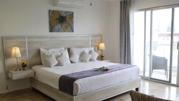 Un dormitorio con una cama grande, dos mesitas de noche con lámparas, un aire acondicionado de pared y un ventanal con vistas.