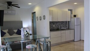 Una cocina moderna con armarios blancos, una mesa de comedor de cristal y un ventilador de techo.