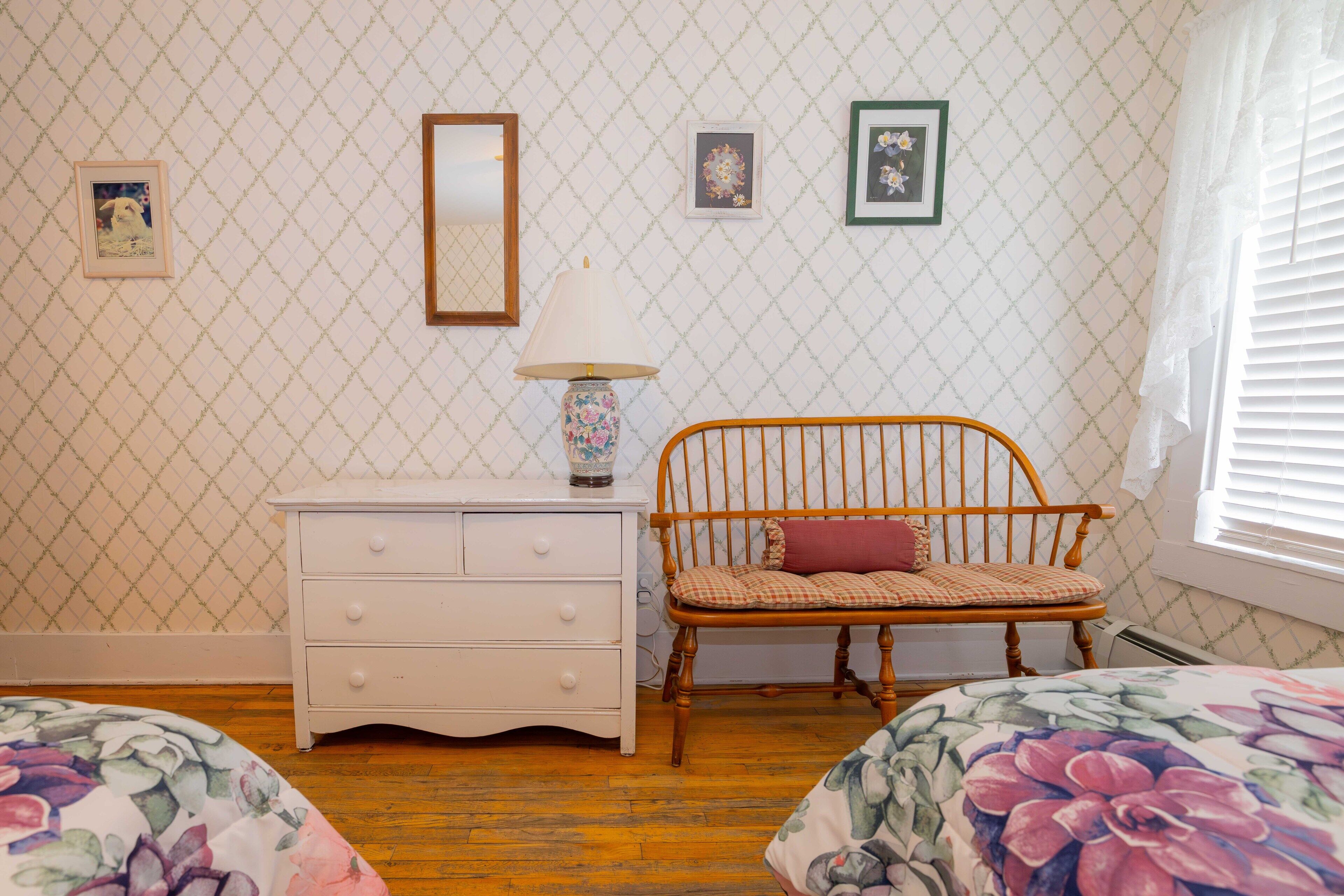 Un dormitorio con cama de madera, cómoda blanca, silla de madera y ventana con persianas.