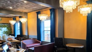 A restaurant interior with wooden flooring, dark walls, and a ceiling with floral patterns. There are several tables and chairs, and a bar area with a counter. - The Hand Hotel (Fairplay)