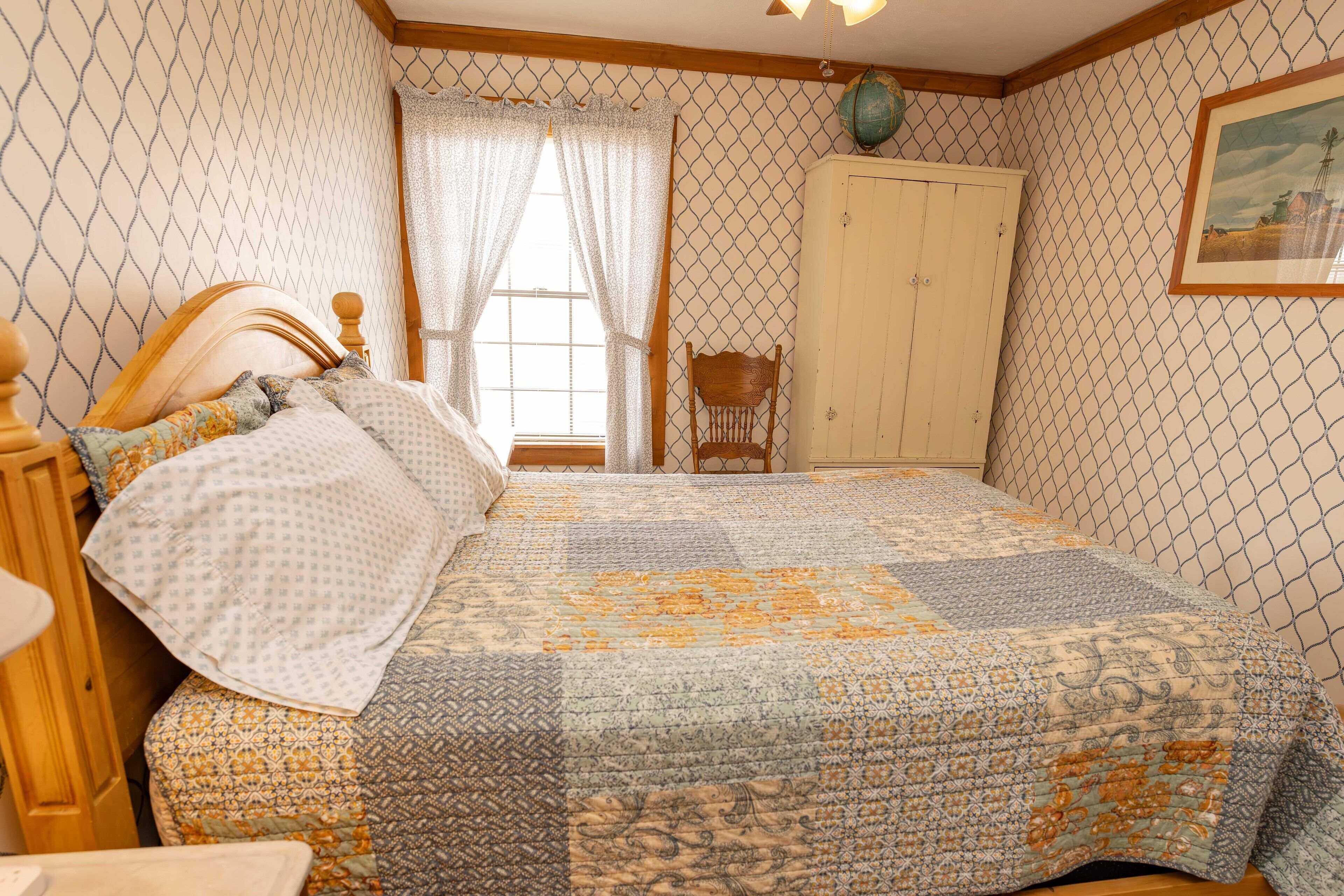 Quarto com cama, cabeceira de madeira, cadeira, guarda-roupa e janela com cortinas.