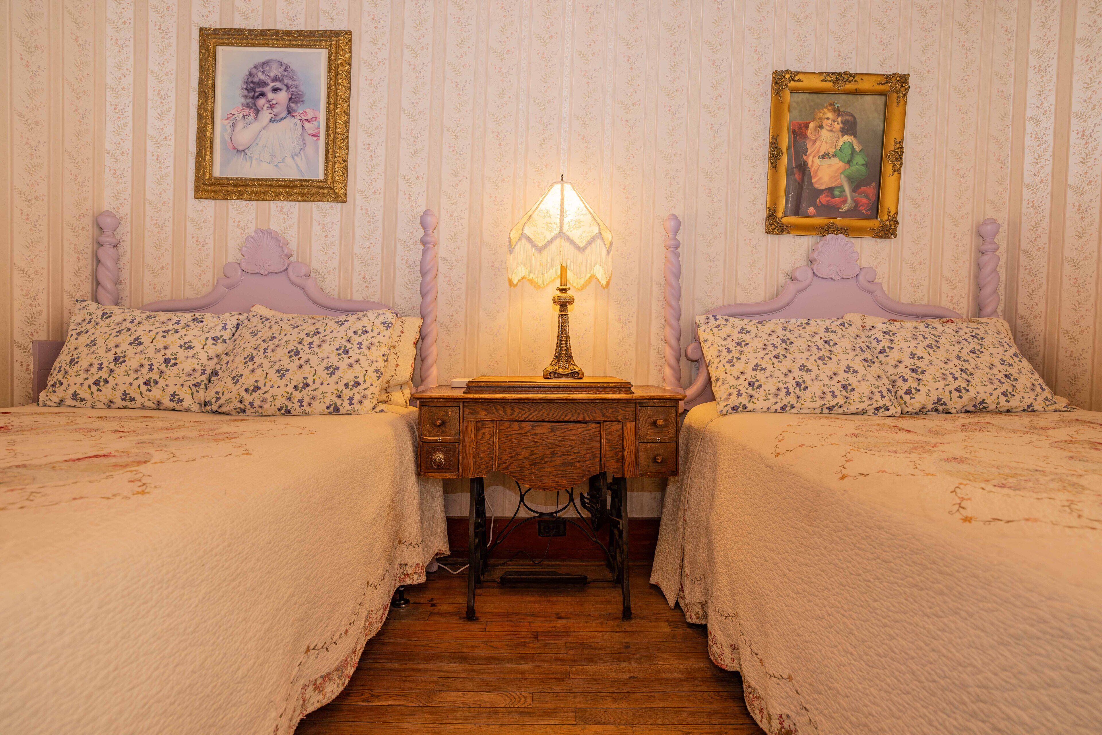 A room with two beds, a wooden desk, and a lamp.