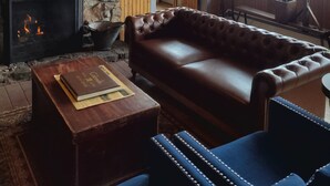 A cozy room with a stone fireplace, leather sofa, and wooden ceiling. - The Hand Hotel (Fairplay)