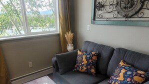 A living room with a grey sofa, patterned cushions, a decorative metal piece above it, and a glass-top coffee table. - The Hand Hotel (Fairplay)