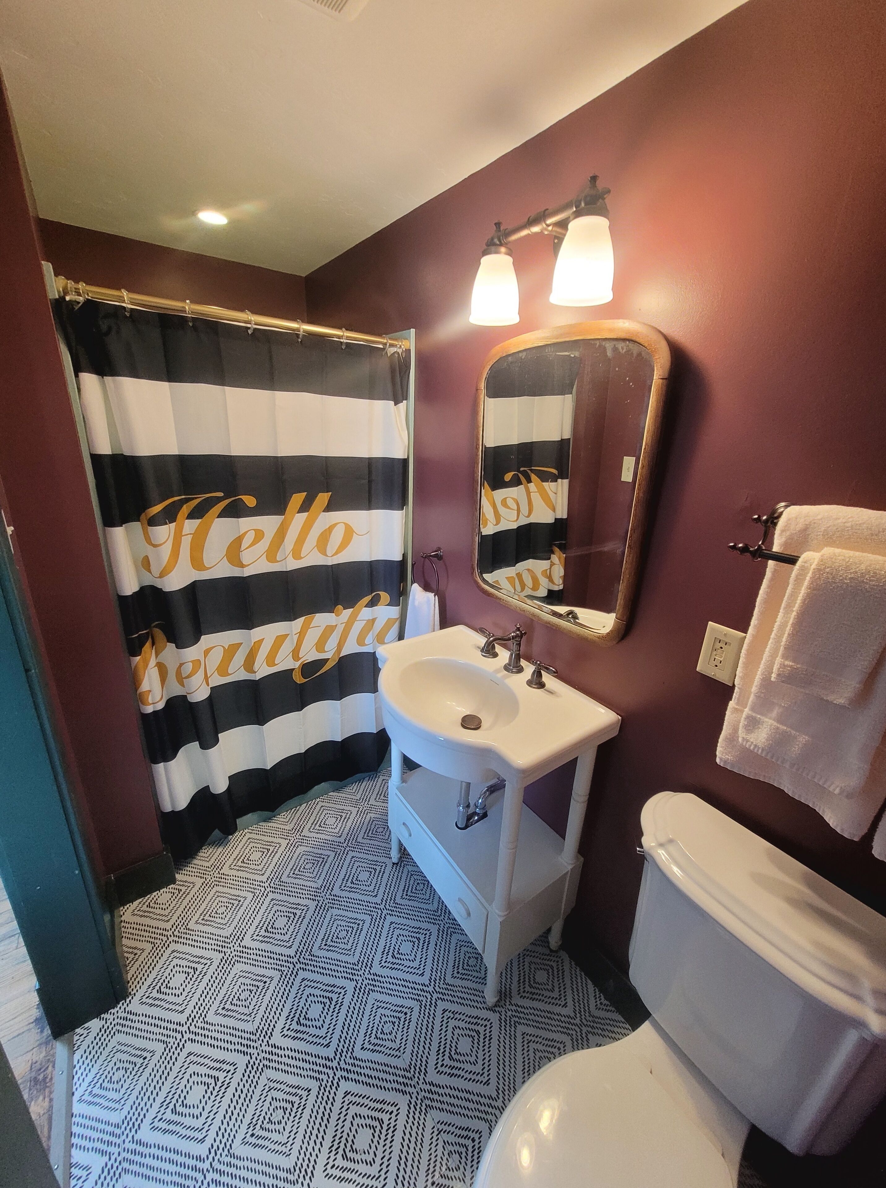 Une salle de bain avec un rideau de douche à rayures, un lavabo, un miroir et des toilettes.
