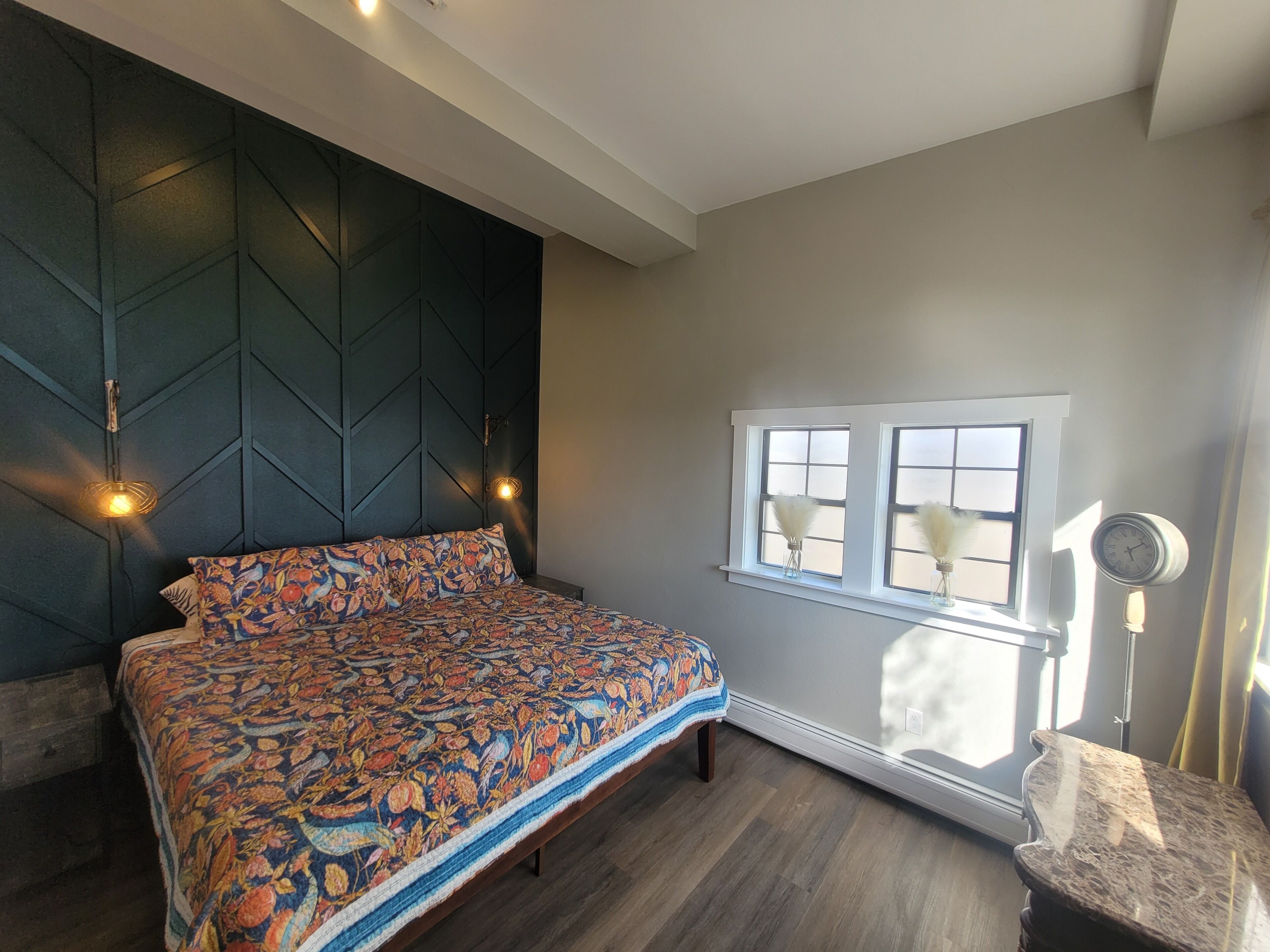 Quarto com cama, janela com cortinas, mesa de cabeceira e luminária na parede.