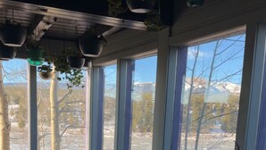 A cozy room with a wooden deck, a cushioned bench, and a view of a snowy landscape through large windows. - The Hand Hotel (Fairplay)