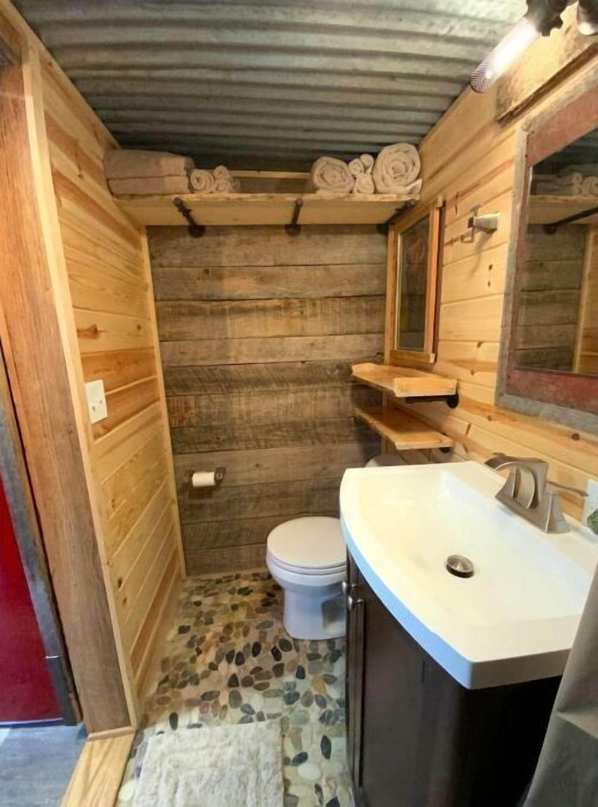Ett litet badrum med träpanel, en vit toalett, ett handfat med spegel och en liten hylla.