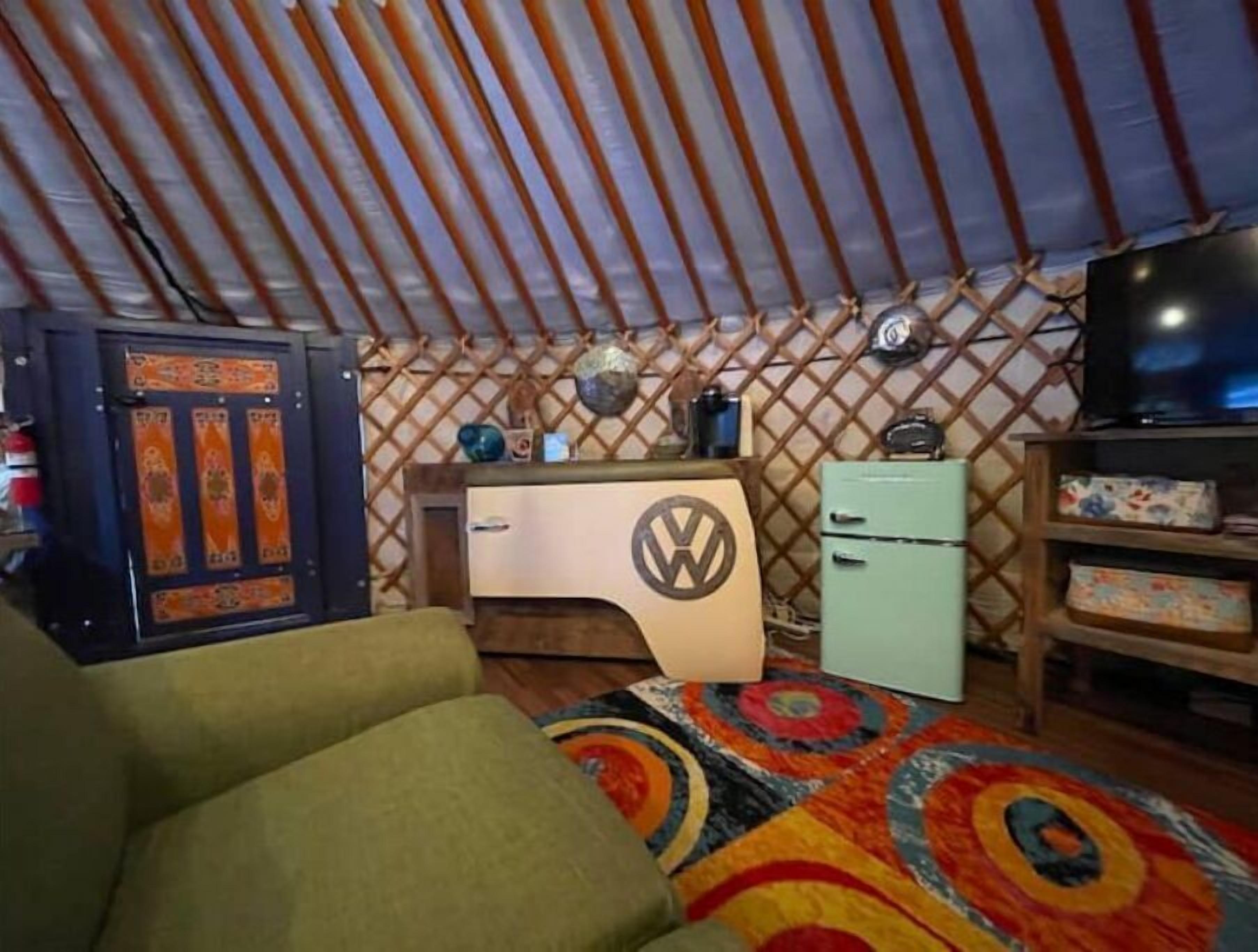 A cozy room with a VW logo desk, a small fridge, a TV, and a colorful rug.