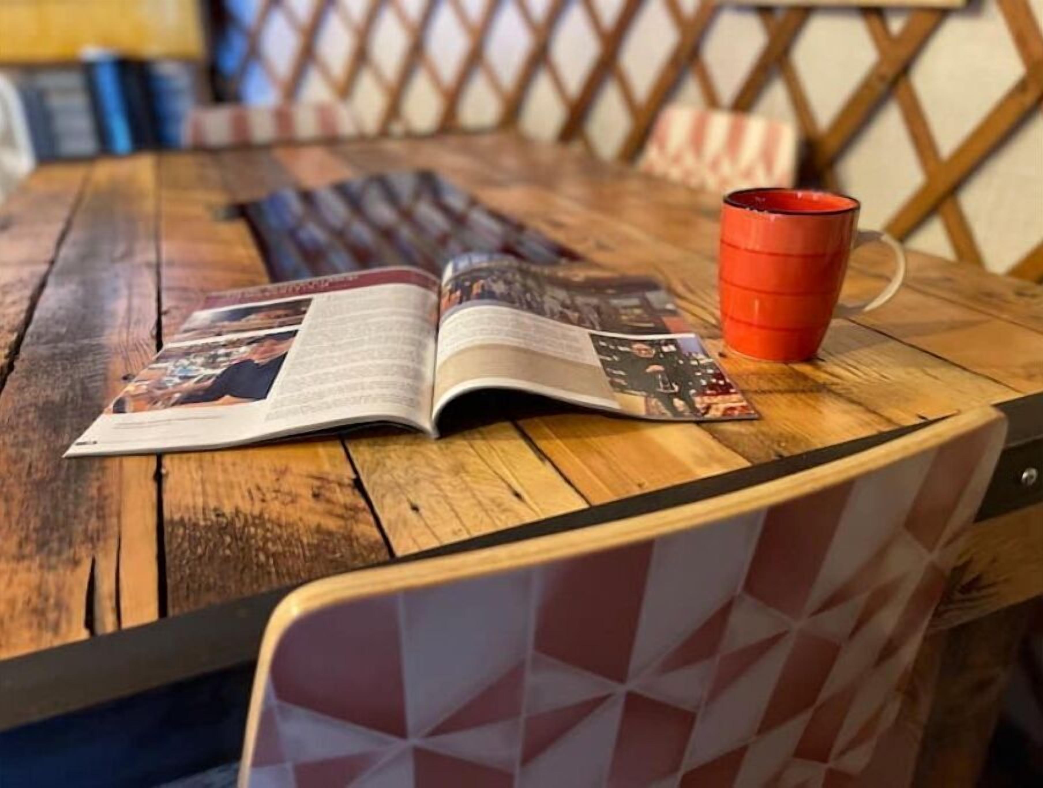 A wooden table with a magazine and a red cup.