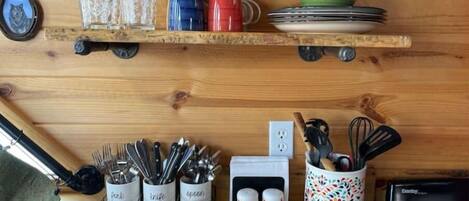 A kitchen with wooden shelves holding colorful cups and plates, utensil holders, and a decorative salt shaker.