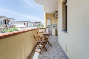 A balcony with a table and chairs, a tiled floor, and a view of neighboring buildings.