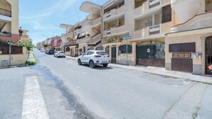 A residential street with multi-story buildings, parked cars, and a clear sky.
