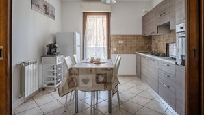 A kitchen with a dining table, chairs, a refrigerator, a coffee machine, and a window with curtains.