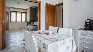 A dining area with a table set for two, a kitchen in the background, and a coffee machine on a cart.
