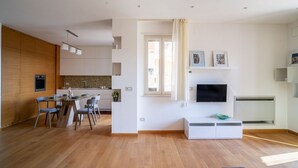 Un salon moderne doté d’un téléviseur à écran plat, d’un coin repas avec des chaises et d’une cuisine avec des meubles en bois.