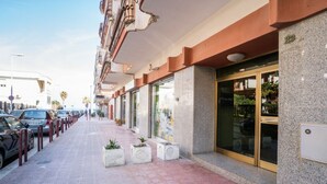 L’entrée d’un hôtel, avec un chemin dallé, des plantes en pot et une porte en verre.