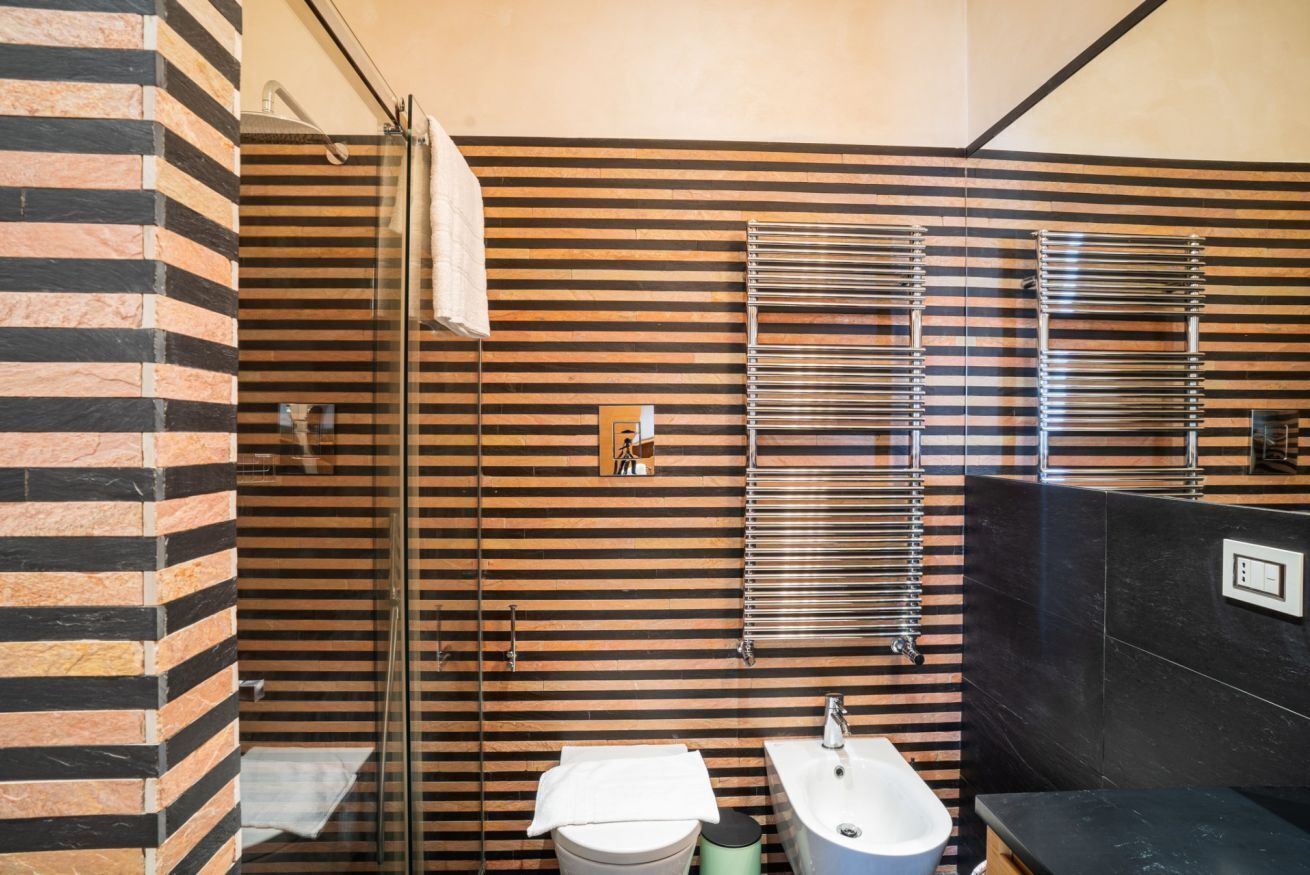 A modern bathroom with a striped wall design, a glass shower enclosure, a white sink, and a bidet.