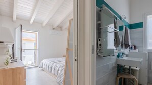 Une chambre à coucher comprenant un lit, une commode en bois, un miroir, ainsi qu’une salle de bain avec un lavabo, un miroir et un porte-serviettes.