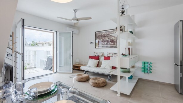 Un salon moderne comprenant un coin repas, un canapé, un ventilateur de plafond et une vue sur l’extérieur grâce à une porte ouverte.