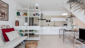 Un salon moderne comprenant un canapé, une table à manger au design épuré, un coin cuisine et un escalier.