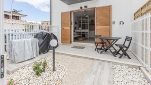Une terrasse extérieure avec une table et des chaises, un barbecue et une clôture blanche.