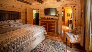 A wooden cabin bedroom with a bed, dresser, TV, and a chair.