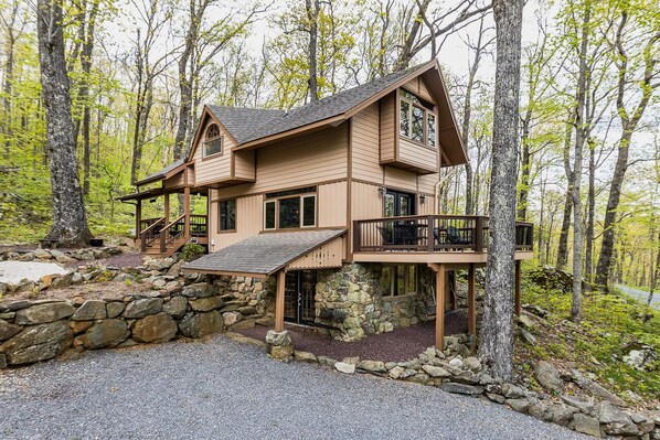Una cabaña con cimientos de piedra, fachada de madera y un balcón con mobiliario exterior.