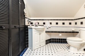 Un baño con suelo de baldosas blanco y negro, un lavabo blanco, un inodoro y un espejo.
