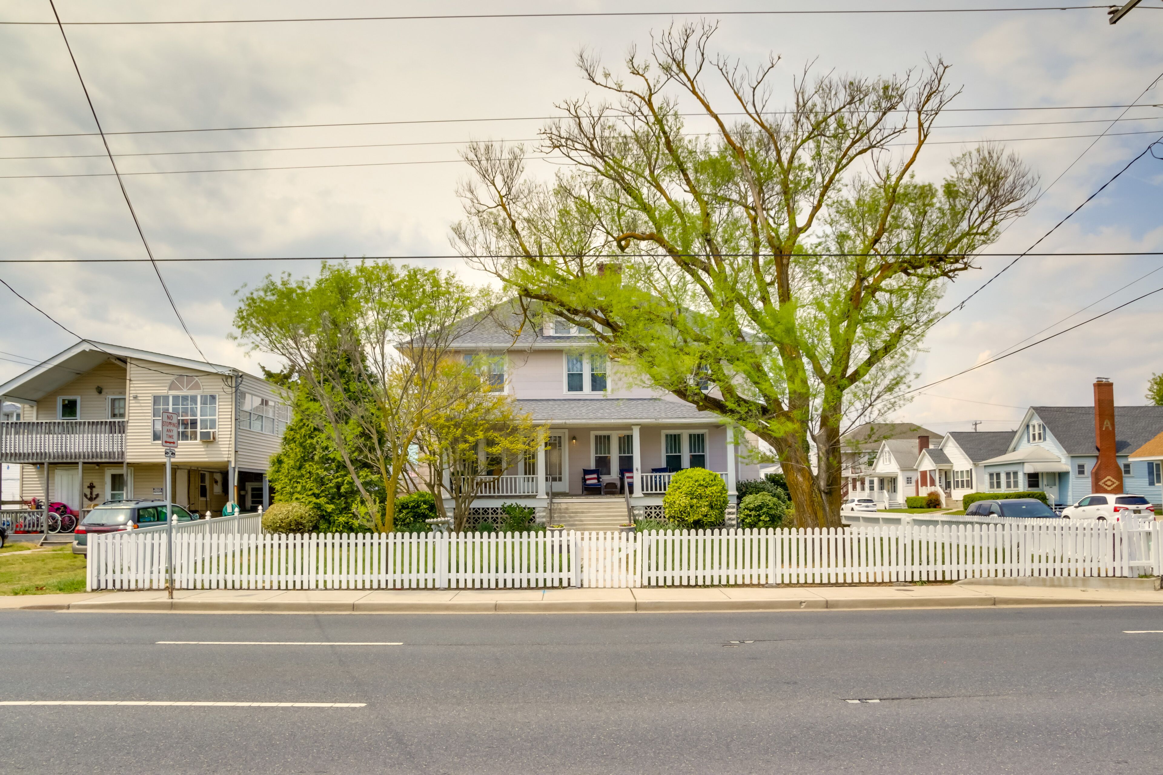 A residential street with houses, a white picket fence, and a clear sky.